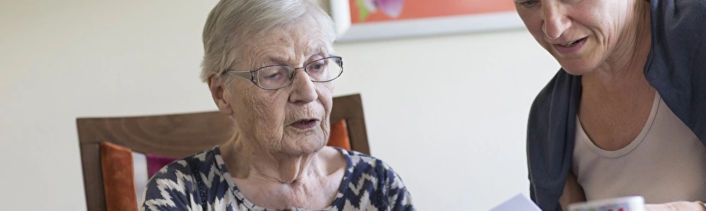 Oudere dame aan tafel leest samen met jongere dame een brief